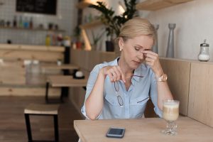 A tired middle aged woman sitting at a table with a coffee cup and cellphone in front of her